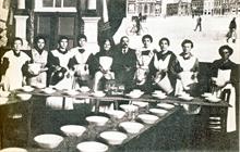Wasmuël : Sous l'occupation. Repas organisé en faveur des enfants durant l'occupation. Bien que le rideau reproduise la Grand-Place de Saint-Ghislain, nous sommes ici à Wasmuël (entre 1914 et 1918)