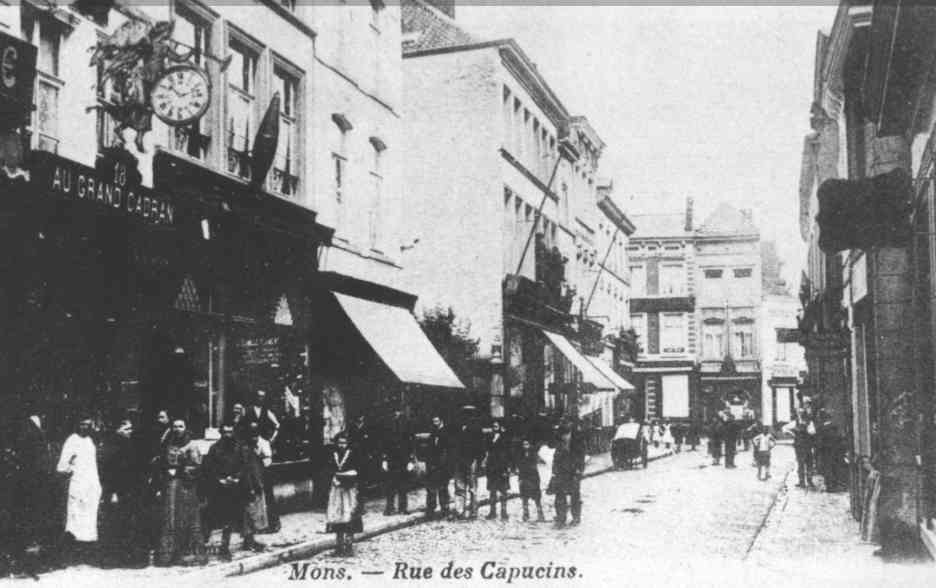 Mons : Rue des Capucins. Nous nous trouvons dans la rue des Capucins. Admirez à gauche la magnifique enseigne de l’horlogerie du Grand Cadran et, à côté, celle bien typique du débit de tabac de Camille Flament. 